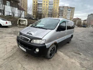 Hyundai Starex 2002 года выпуска, темно-серого цвета, госномер А775ТС51. VIN: KMHWP81HP2U462398. Многочисленные трещины на заднем бампере. Глубокая коррозия металла, в том числе и сквозная, в области колесных арок. Вмятины, следы ржавчины присутствуют по всему кузову ТС. Трещины на лобовом стекле…