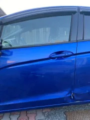 Honda Fit 2013 года выпуска, VIN кузова GK31020913 (GK3-1020913). Автомобиль после ДТП: глубокие вмятины и деформация левой передней двери (требуется замена), вмятины и царапины левой задней двери (требуется ремонт и покраска), вмятины порога с левой стороны. Царапины и сколы краски по всему…